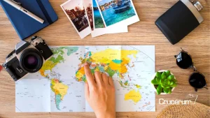 Persona señala con la mano en un mapa sobre una mesa en la que hay una cámara fotográfica, unas fotos gafas y un pasaporte como prepararte para una vuelta al mundo crucerum